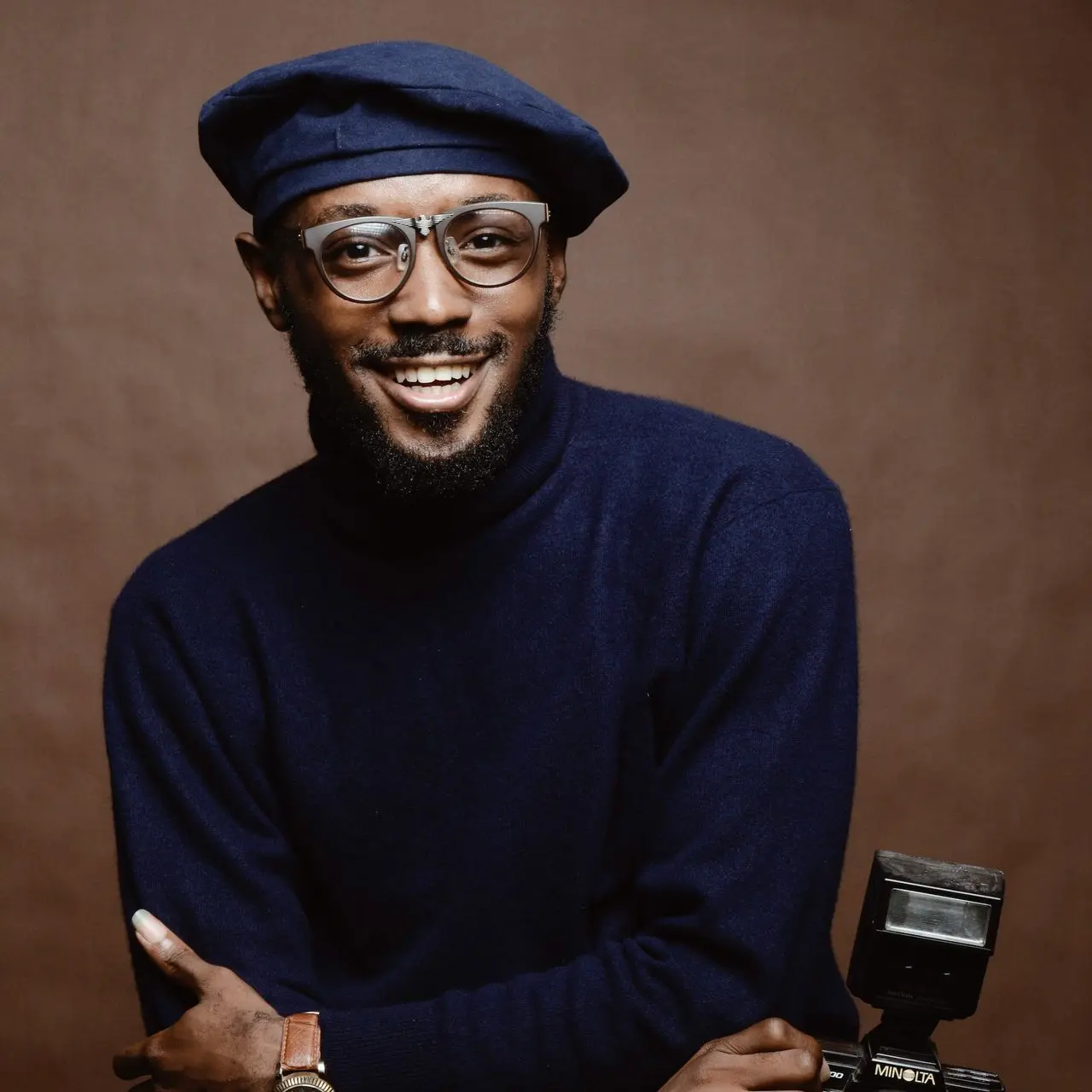 un hombre sonriente usando una camisa negra con cuello alto sosteniendo una cámara
