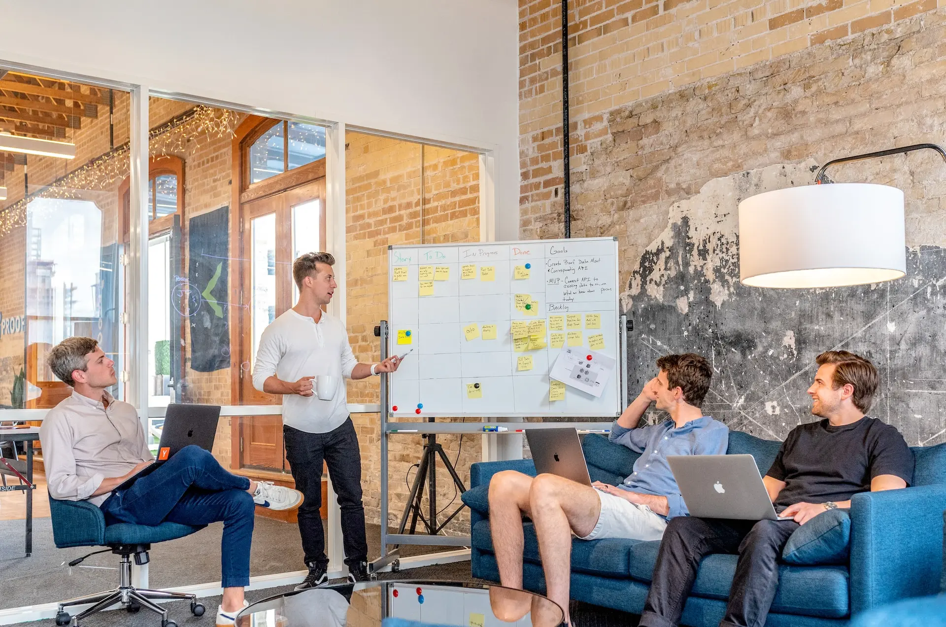 tres hombres sentados mientras usan computadoras portátiles y miran al hombre que está junto al pizarrón