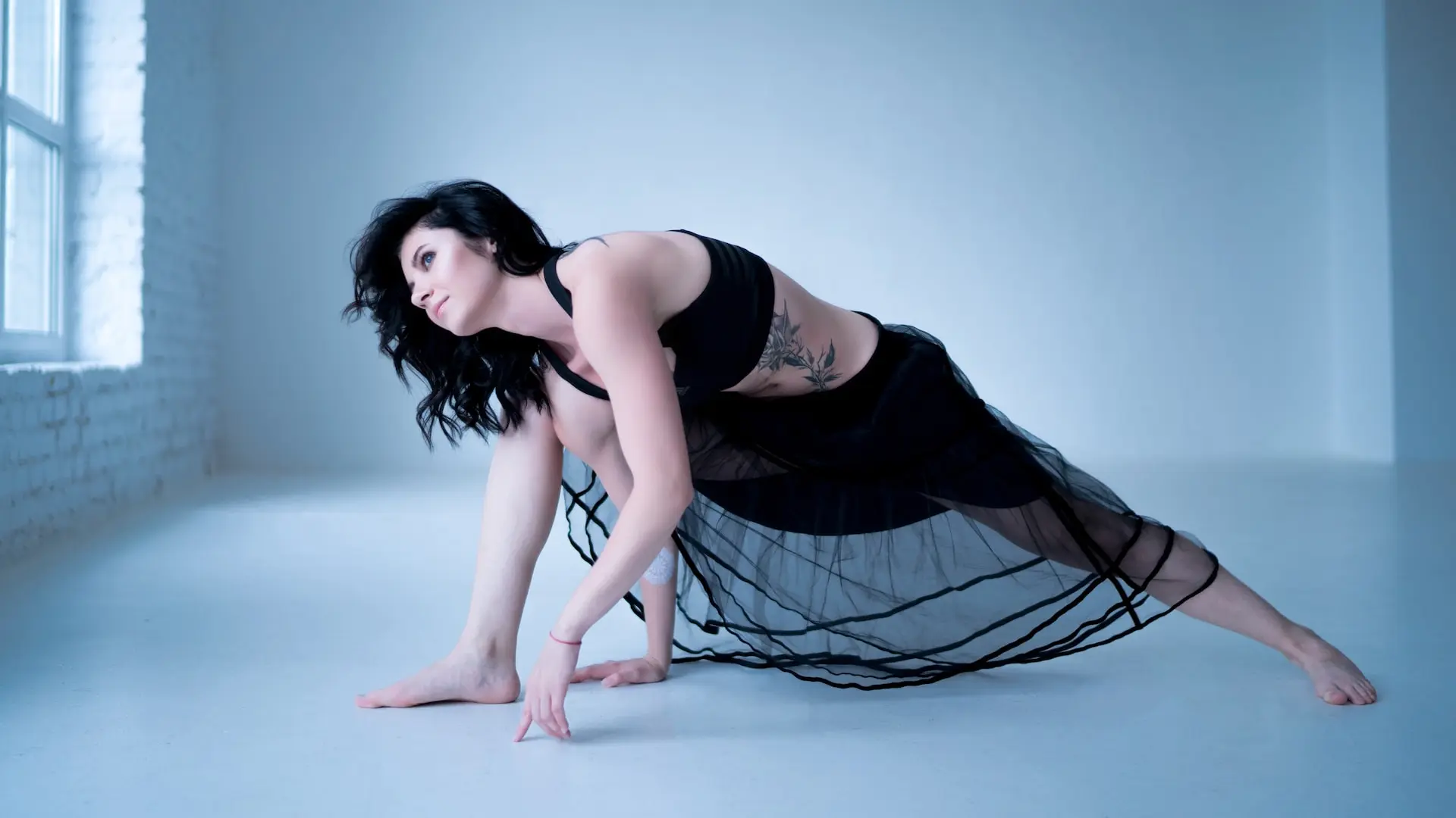 una mujer usando una playera negra y una falda negra con blanco acostada sobre el piso azul