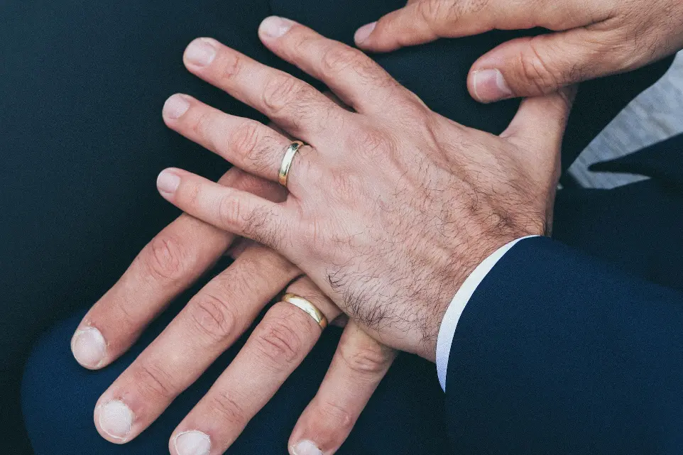 dos manos de hombre que llevan anillos de boda de color oro